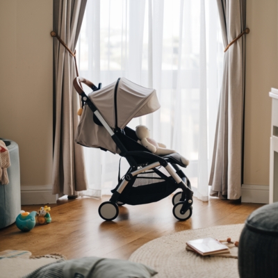 Lightweight beige stroller with a foldable design, placed in a cozy living room, ideal for small spaces and easy storage.