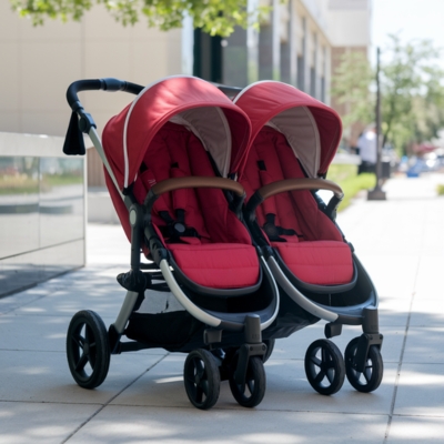Vibrant red double stroller with side-by-side seating and leather-accented handles, designed for siblings, perfect for city walks and outdoor outings.