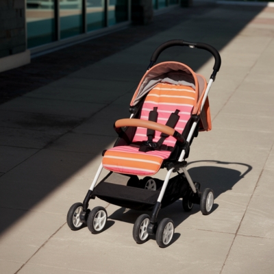 An orange and white striped lightweight stroller sits on a sunlit sidewalk, highlighting its compact design and ease of use for maximizing stroller convenience.